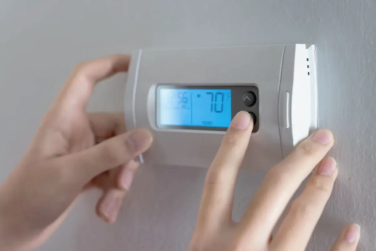 Hands adjusting a digital wall thermostat